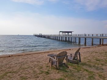 Broken chairs with pier over sea against sky