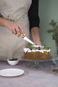 The girl's hands are cutting the christmas cake with red berries on a gray table.