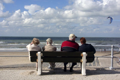 Rear view of people sitting on bench looking at sea