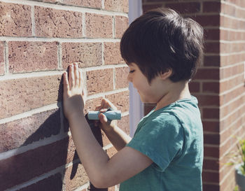 Side view of smiling boy writing on brick wall
