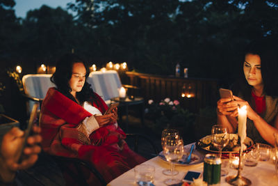 Female friends using mobile phones at table during dining party