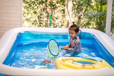 Cute little girl playing in an inflatable rubber swimming pool at home during quarantine period.