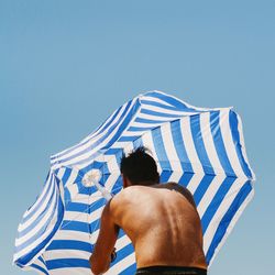 Low angle view of person holding beach umbrella against clear blue sky