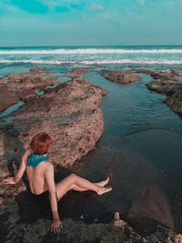 Woman relaxing on rock at beach against sky