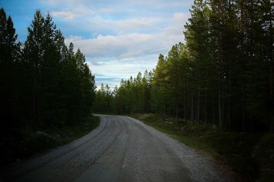 Country road amidst trees against sky