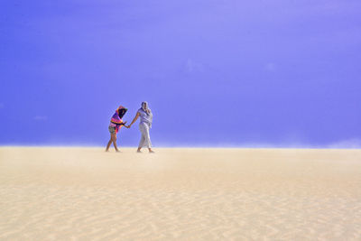 People on sand dune on desert against sky