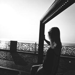 Woman sitting on railing by balcony against clear sky