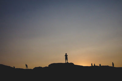 Silhouette people standing on land against clear sky at sunset