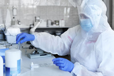 Woman scientist wearing protective costume, screen, gloves working in laboratory making a covid test