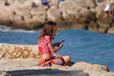 Woman sitting on rock by sea