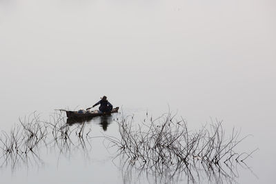 Men sitting on boat in lake against sky