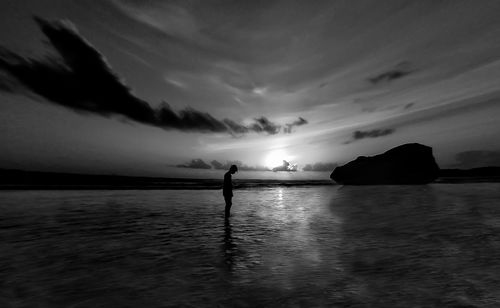 Silhouette person standing in sea against sky during sunset