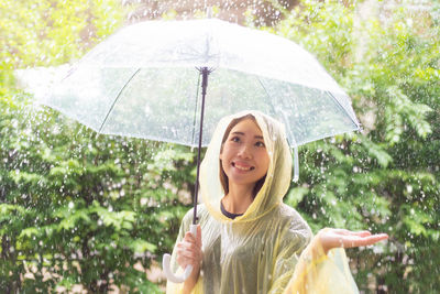 Young woman holding umbrella while standing against plants during rain