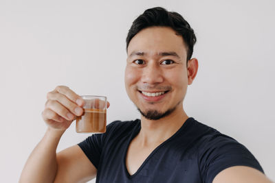 Portrait of young woman holding drink against white background