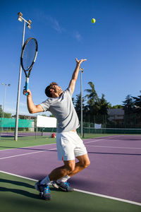 Man playing tennis on court against blue sky