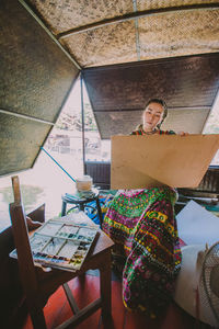 Young woman painting on cardboard while sitting indoors