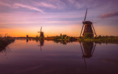 Traditional windmills at lakeshore against sky during sunset