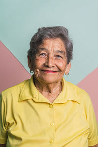 Elderly female with short gray hair and brown eyes looking at camera on pink and blue background in studio