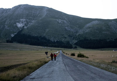 Rear view of people walking on road leading towards mountain