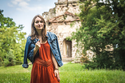 Portrait of smiling young woman standing against old building and trees