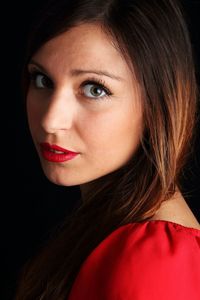 Close-up portrait of young woman with red lipstick against black background