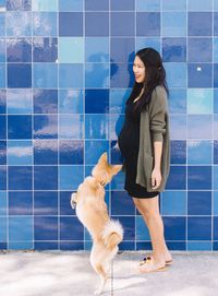 Smiling pregnant woman with dog by blue wall