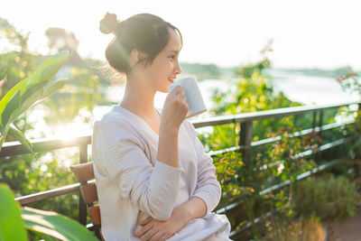 Side view of young woman standing against railing