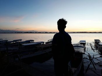 Rear view of silhouette man standing by sea during sunset