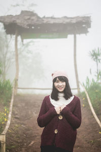 Portrait of smiling young woman standing against trees during winter