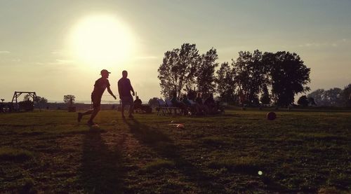 Silhouette people on field against sky during sunset