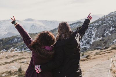 Rear view of female friends with arms raised standing against mountains