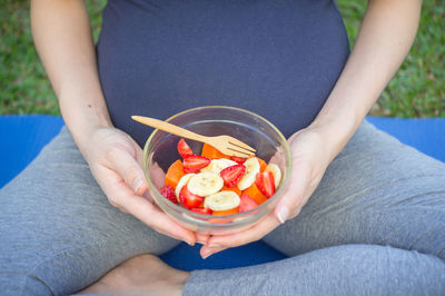 Midsection of pregnant woman eating fruits in bowl