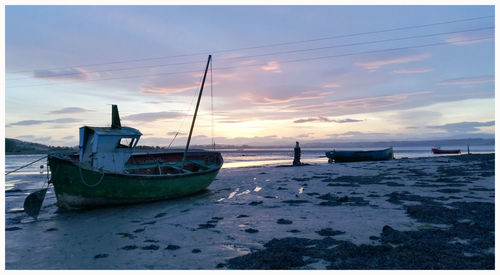 Boat moored on beach against sky during sunset