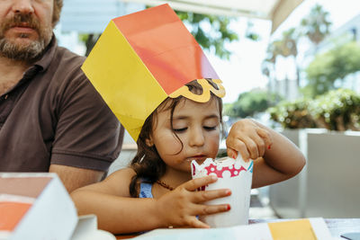 Cute girl eating ice cream while sitting with father at restaurant