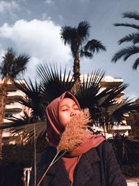 Young man standing by palm tree against sky