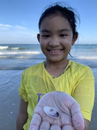 Portrait of cute girl holding seashell standing at beach
