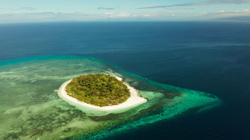 Tropical island mantigue and sandy beach surrounded by atoll coral reef and blue sea, aerial view. 