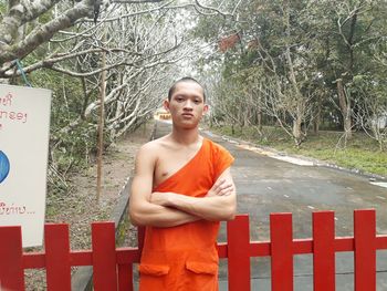 Portrait of man standing by fence against trees