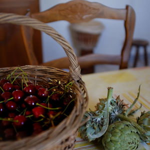 Close-up of cherries in basket by artichoke on table