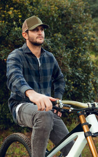 Mountain biking sportsman without protection sitting on bike in the middle of a forest looking away
