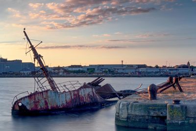 Abandoned boat in sea against sky during sunset