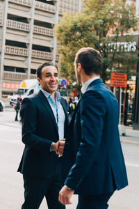 Smiling mature businessman greeting male colleague on street in city