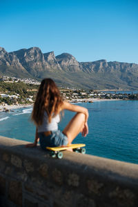 Woman sitting against mountains against clear blue sky