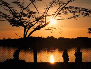 Silhouette people by lake against sky during sunset