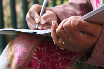 Midsection of woman writing on book while sitting outdoors