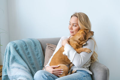 A young beautiful woman in casual clothes hugs and pets her beloved dog sitting