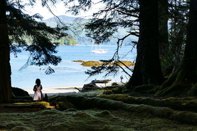 Man sitting on tree by lake against sky