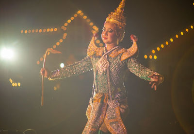 Portrait of smiling woman standing by illuminated lights at night