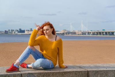 Young red-haired girl in yellow sweater and jeans. pretty woman sits