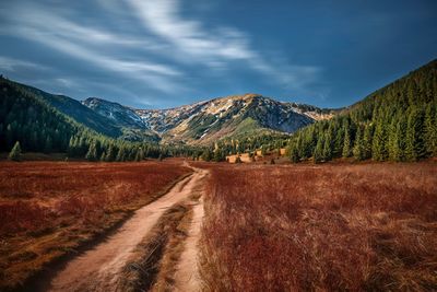 Dirt road by mountains against sky